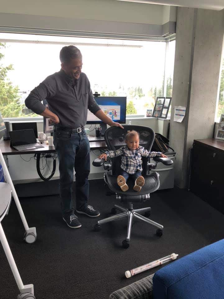 Rajesh smiling at a baby sitting in his office chair