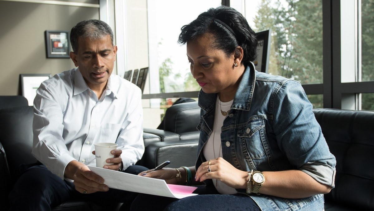 Genise and Rajesh reviewing documents together on an office couch