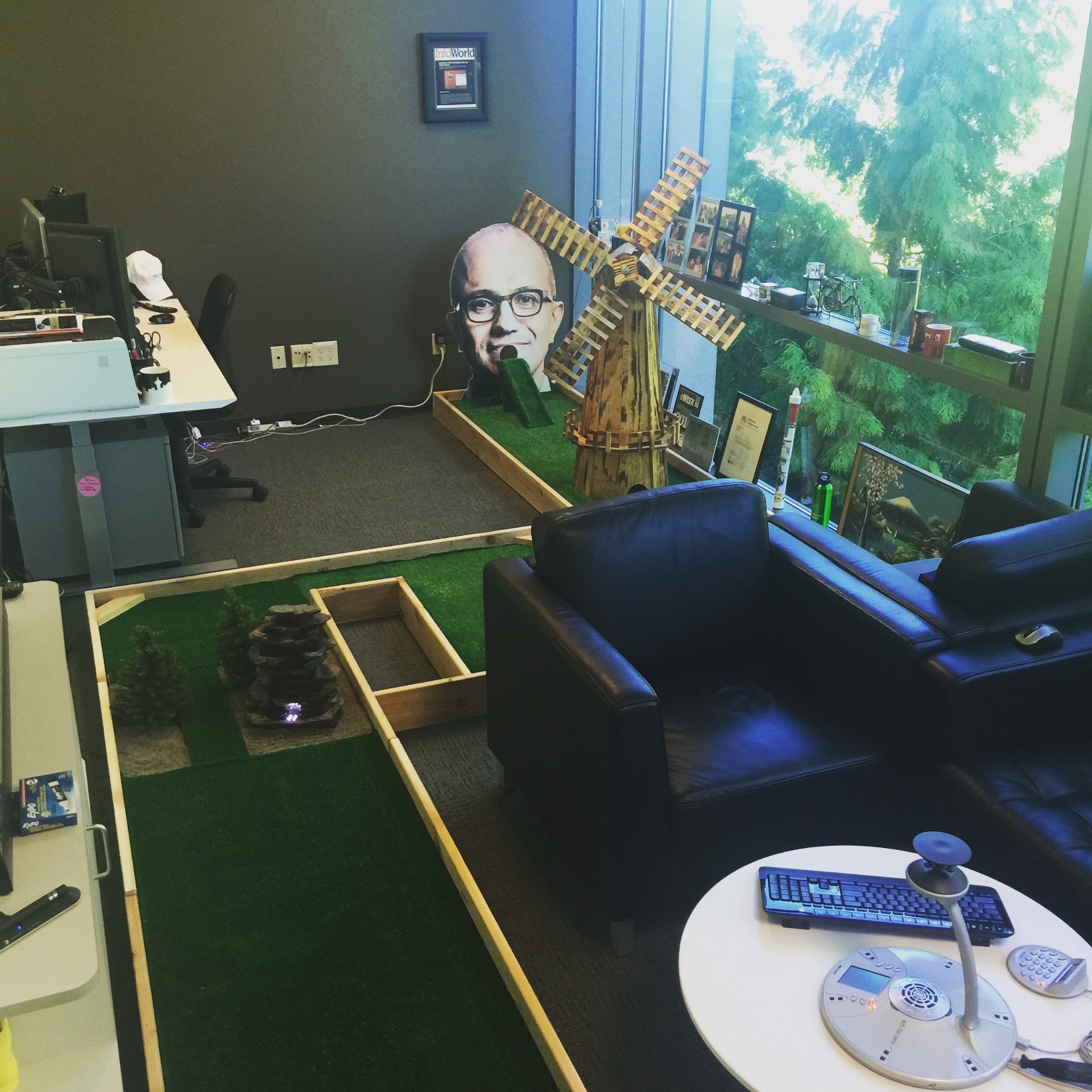A mini golf course with turf, wooden borders, a windmill, and a waterfall built inside Rajesh's office