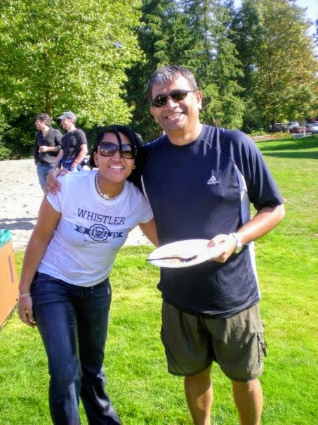Genise and Rajesh outdoors in sunglasses at a team event